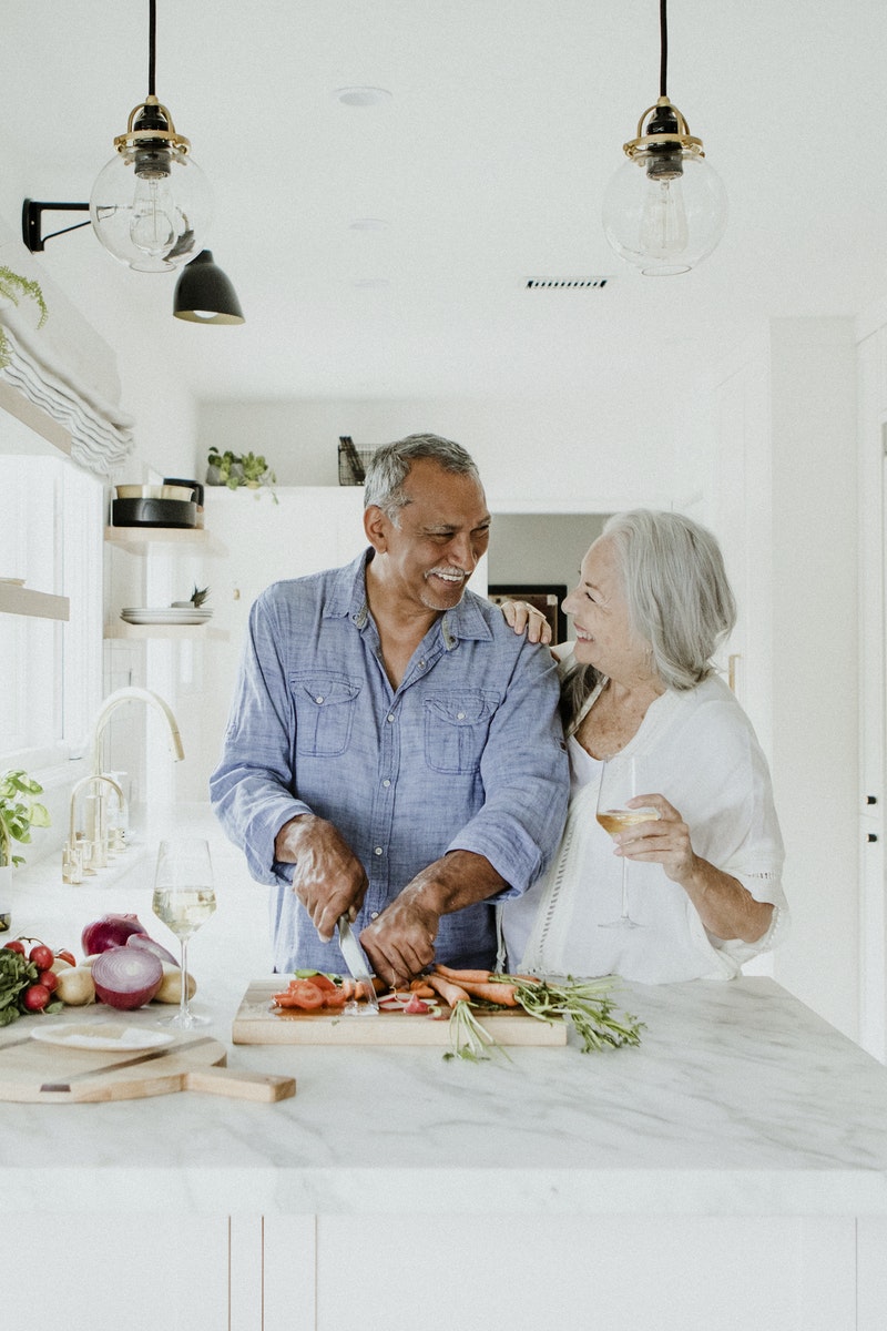 Couple laughing while cutting vegetables in kitchen