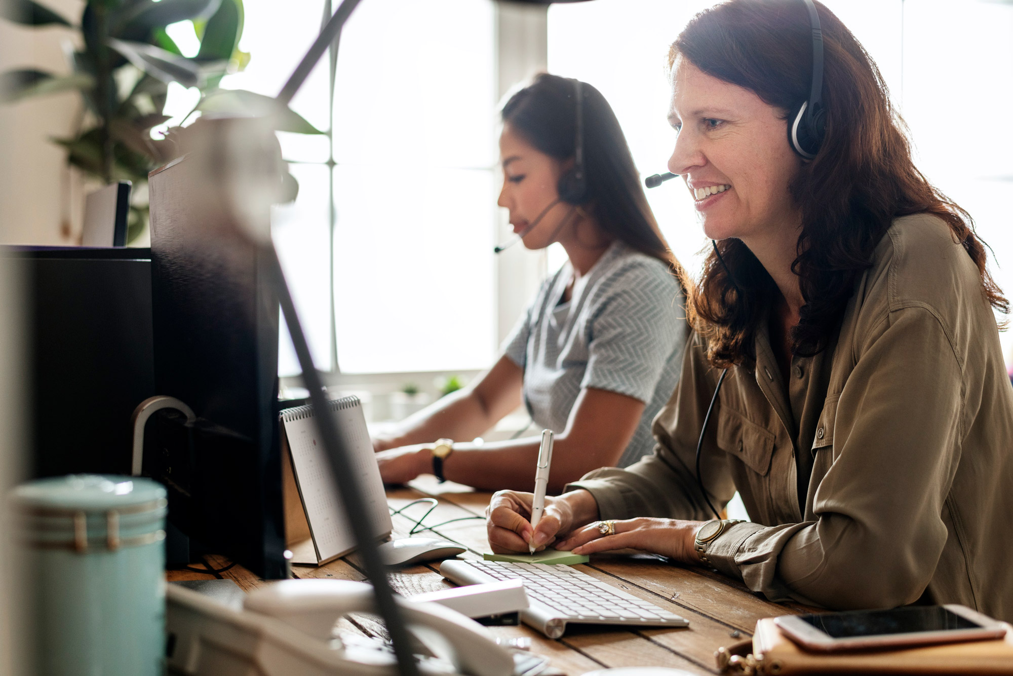 Two people with headsets taking calls at a desk