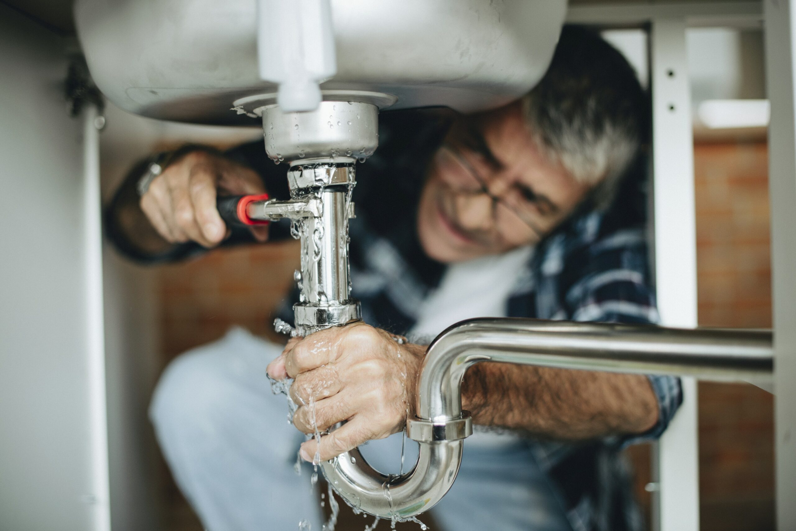 Man trying to fix leaking pipes below sink