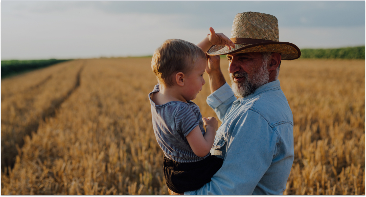 Farmer standing in field of wheat holding his grandson